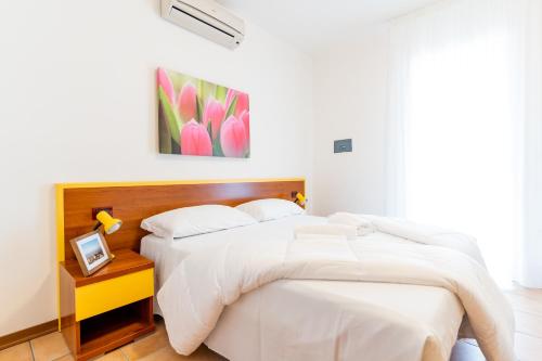 a white bedroom with two beds and a picture on the wall at Pini Village Lido Altanea in Caorle