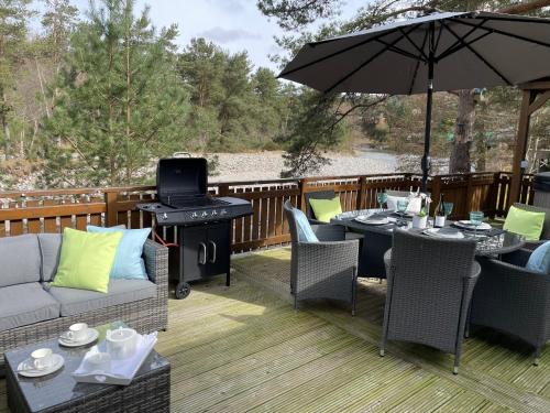 a patio with tables and chairs and an umbrella at Luxury Riverside Lodge, Blair Atholl in Pitlochry