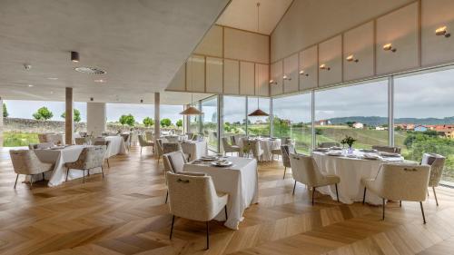 Un restaurante con mesas y sillas blancas y grandes ventanales. en CoolRooms Palacio de Luces, en Luces