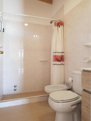 a white bathroom with a toilet and a shower at APA Coralillos - complejo de cabañas con parrillas y estacionamiento cubierto in Puerto Madryn