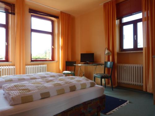 a bedroom with a bed and a desk and two windows at Waldhaus Colditz Garni in Colditz