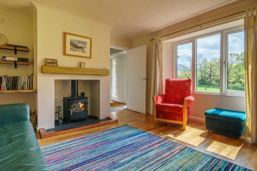 a living room with a fireplace and a red chair at Cherry How - Patterdale - Dog-friendly in Patterdale