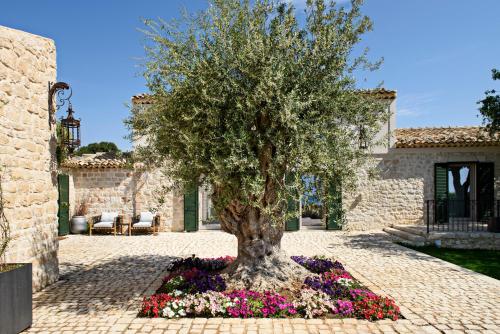 a tree in a bed of flowers in front of a house at Poggio Leano Boutique Hotel in Donnalucata