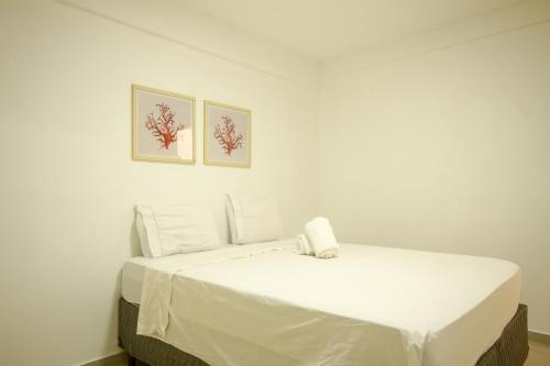 ein weißes Bett in einem Zimmer mit zwei Bildern an der Wand in der Unterkunft Venha curtir essa maravilha! Frente para o mar! in Angra dos Reis