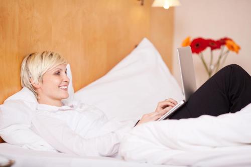 a woman laying on a bed with a laptop at Hotel Bockelmann in Bispingen