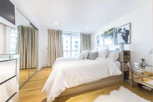 a white bedroom with a large bed and windows at Panoramic Riverside Facing - 2 Bed - 2 Bath - 2 Balconies - London Nine Elms in London