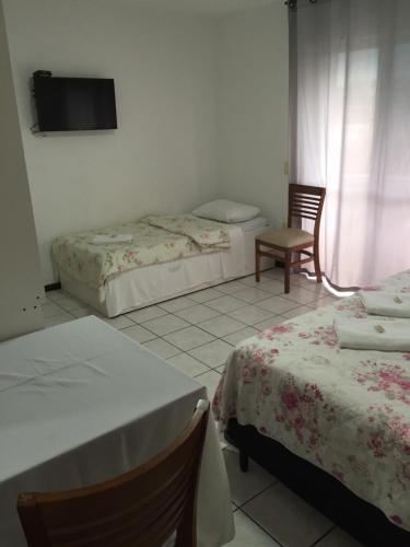 a room with two beds and a tv on the wall at Vila Alaide Praia Hotel in Barra Velha