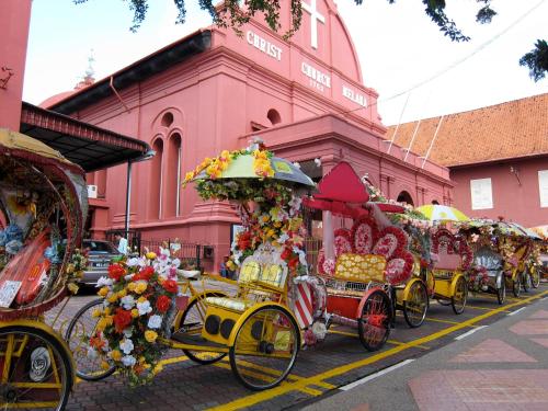 a row of horse drawn carriages parked in front of a pink building at Hallmark Express Hotel in Melaka