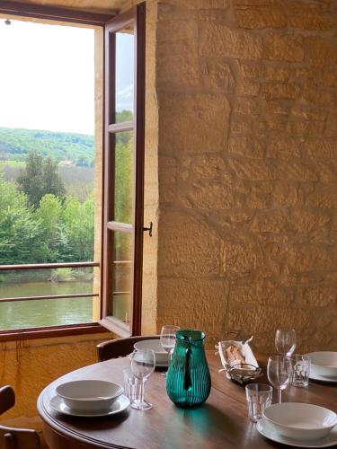 une table en bois avec un vase vert et une fenêtre dans l'établissement Les Courtines - Appartement de caractère à la Roque-Gageac - Les Lauriers, à La Roque-Gageac