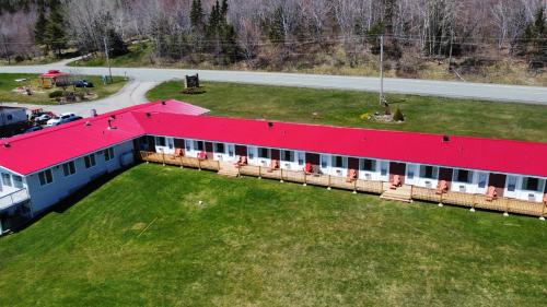 a building with a red roof on a grass field at Trailsman Lodge in Baddeck