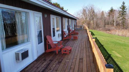 a porch of a house with red chairs on it at Trailsman Lodge in Baddeck