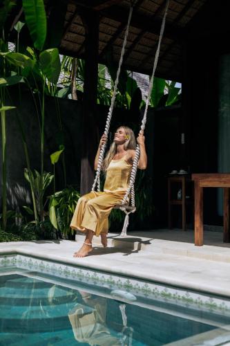 a woman sitting on a swing by a swimming pool at Jati Kuta Lombok in Kuta Lombok