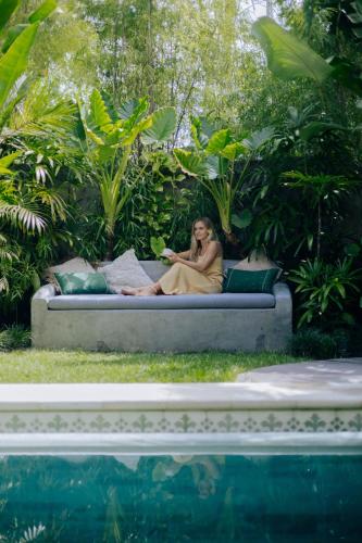 a woman sitting on a couch next to a pool at Jati Kuta Lombok in Kuta Lombok