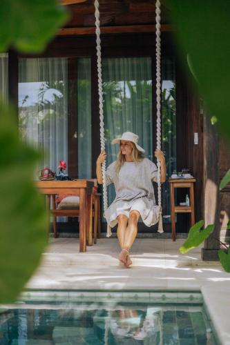a woman sitting on a swing by a pool at Jati Kuta Lombok in Kuta Lombok