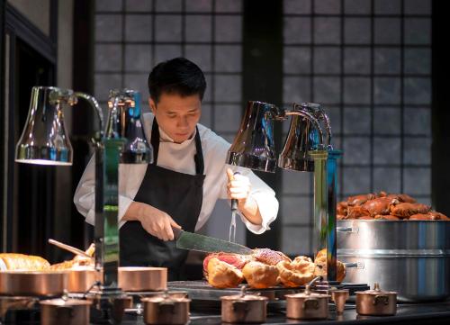 a man in a kitchen preparing food on a grill at The Landmark Bangkok in Bangkok