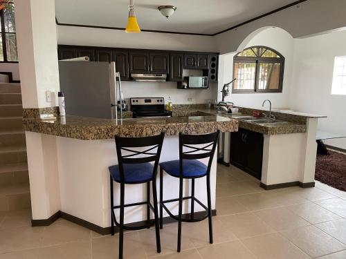 una cocina con 2 taburetes en una barra de cocina en Family oriented house just steps to the beach, en Jacó