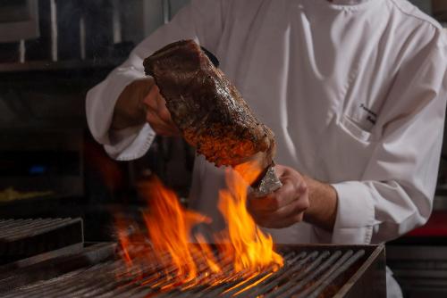 a man holding a piece of meat on a grill at The Landmark Bangkok in Bangkok