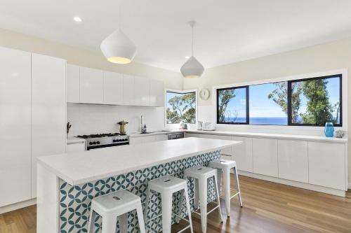 Una cocina con gabinetes blancos y una encimera con taburetes. en Vue Sur La Mer, en Wye River