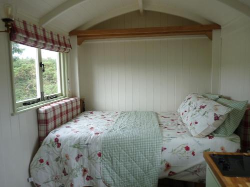 a small bedroom with a bed and two windows at Shepherds Hut on Cornish Smallholding in Penzance