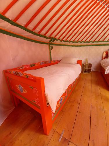 uma cama laranja num quarto com piso em madeira em A Ventoux Yourte em Monieux