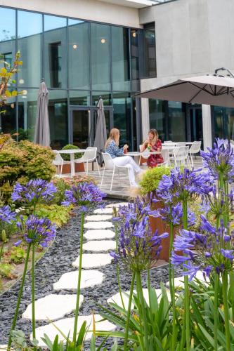 two women sitting at tables in a garden with purple flowers at Novotel Le Havre Centre Gare in Le Havre