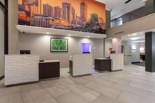 a lobby with three counters and a painting of a city at La Quinta by Wyndham Boston-Andover in Andover