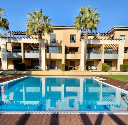 a swimming pool in front of a building with palm trees at Janelas do Oceano - Casa de Ferias T3 Vilamoura in Vilamoura