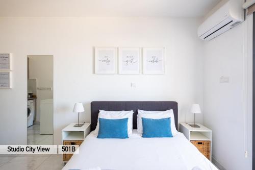 a white bedroom with a bed with blue pillows at Lazuli City & Seaview Apartments in Larnaca