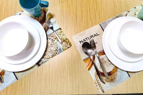 a table with white plates and silverware on a napkin at Almas Muji Studio 100mbps Netflix STAY in Nusajaya