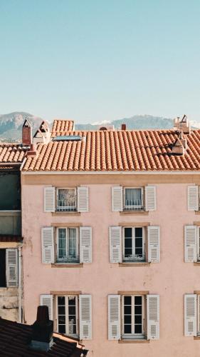 a pink building with white windows and mountains in the background at Hotel San Carlu Citadelle Ajaccio in Ajaccio