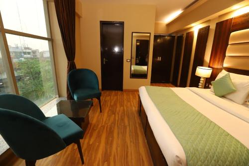 a hotel room with a bed and chairs and a window at Hotel Palm Grand Naraina New Delhi - Couple Friendly Local IDs Accepted in New Delhi
