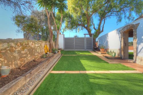 einen Garten mit grünem Gras und einer Steinmauer in der Unterkunft Villa Can Roig by Hello Homes Sitges in Sant Pere de Ribes