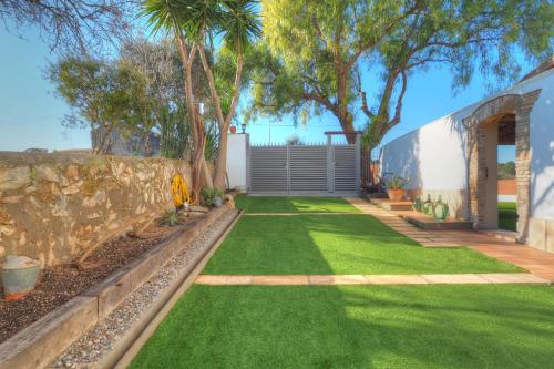un jardín con césped verde y una pared de piedra en Villa Can Roig by Hello Homes Sitges, en Sant Pere de Ribes