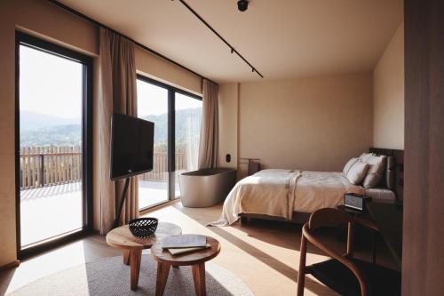 Schlafzimmer mit einem Bett, einem TV und einem großen Fenster in der Unterkunft Boutiquehotel DAS ZEITWERT in Deutschlandsberg