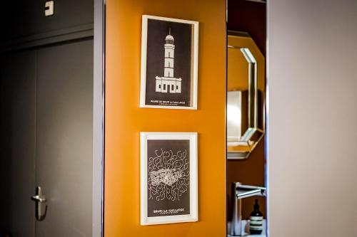 two framed pictures of a lighthouse on an orange wall at Hôtel Le Collonges TV connecté wifi Netflix in Brive-la-Gaillarde