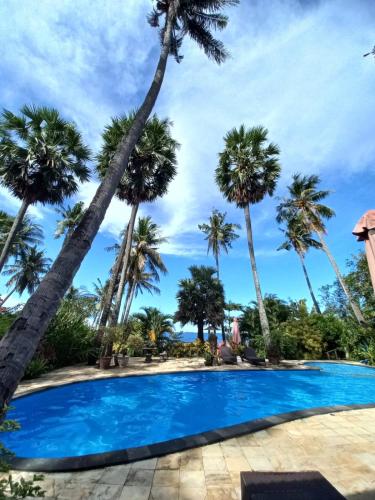 a pool with palm trees in the background at Bali North Beach Villa - Ocean Front in Tianyar