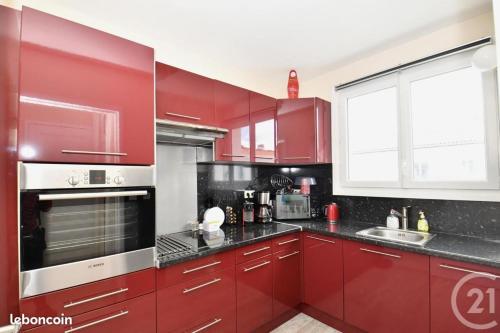 La cuisine est équipée de placards rouges et d'un four en acier inoxydable. dans l'établissement Appt cosy 65 m2 coeur de ville à 150 m de la plage, à Royan