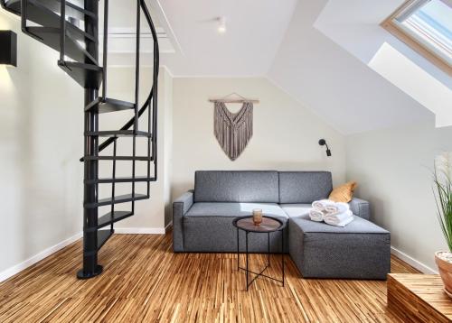a living room with a gray couch and a spiral staircase at Apartament Piaskowy in Chmielno