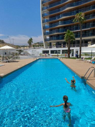 two people swimming in a large swimming pool at SUNSET WAVES blue sky apartment in Benidorm