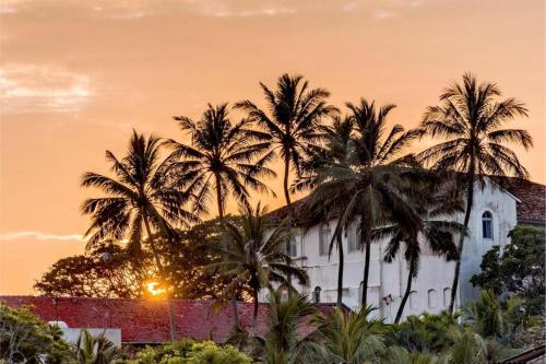 a building with palm trees in front of a sunset at The Entrance Galle Fort in Galle