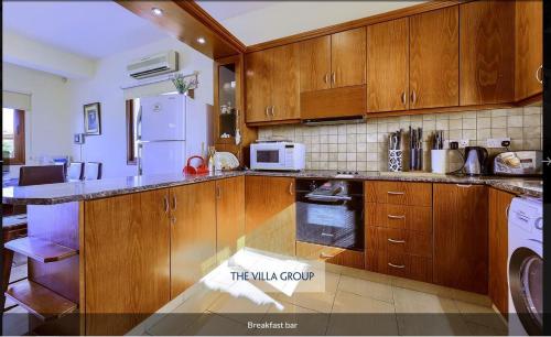 a kitchen with wooden cabinets and a white refrigerator at Nayia Paradise Villa! Best Villa in Cyprus in Paphos City