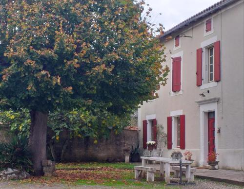 a picnic table under a tree next to a white building at Gites les Lignons in Champniers