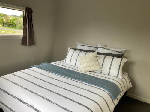 a bed with white and blue sheets and a window at Kiwi beach bach in Riverton