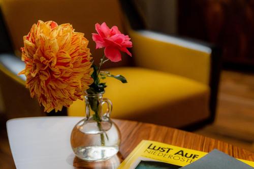 a vase with flowers on a table next to a book at Grüner Baum Wachau - Retro Frühstückspension in Mautern