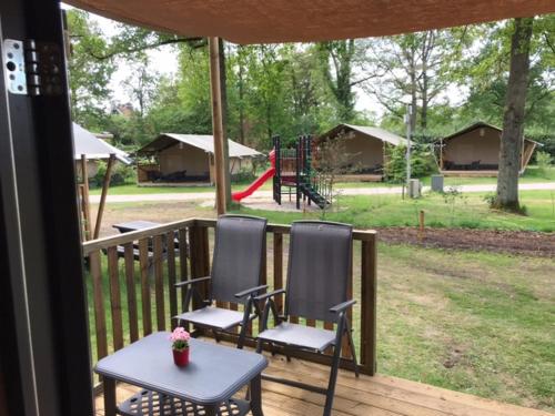 twee stoelen en een tafel op een veranda met een speeltuin bij Tiny House de Wood Lodge in Ootmarsum