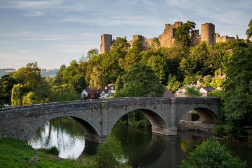 un pont sur une rivière avec un château en arrière-plan dans l'établissement Topsy-Turvy, Gardeners Cottage, Clungunford, Ludlow, Shropshire SY70PN, à Broome