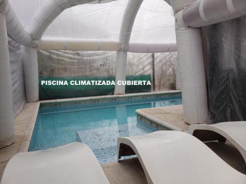 una piscina con 2 sillas blancas al lado en UNICA Casa Centro frente al lago, pileta climatizada, 4 dorm, 3 baños, 3 autos, aire, en Villa Carlos Paz