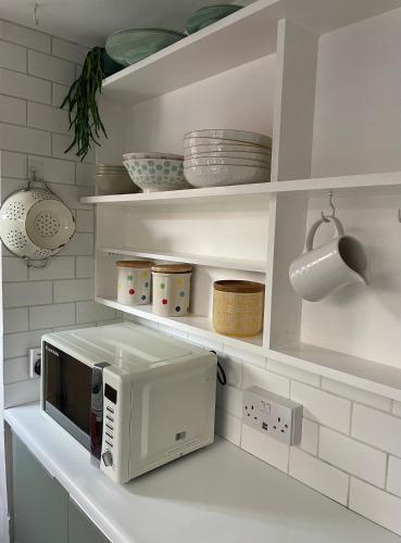 a white kitchen with a microwave on a shelf at Cosy 2 bedroom Victorian cottage, Newport, Isle of Wight in Newport