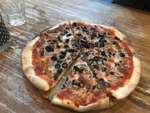 a pizza with black olives on a wooden table at Blu oceano B&B, Italian restaurant in Nembrala