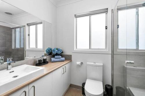 a white bathroom with a sink and a toilet at CASA EMEC- luxury, aircon, walk to the shops and beach! Outdoor shower and garage parking in Ocean Grove